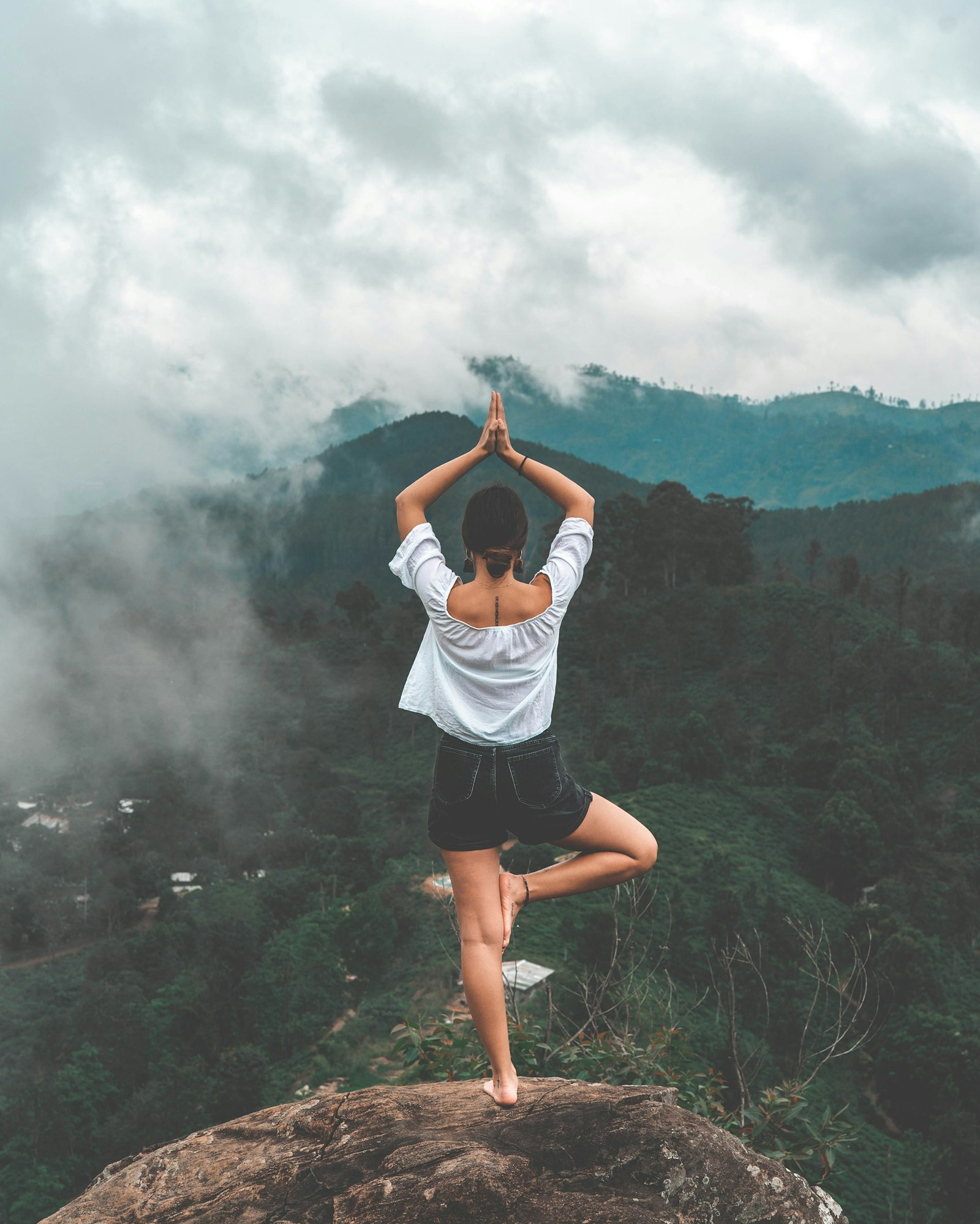 A practitioner in tree pose facing mist-covered mountains